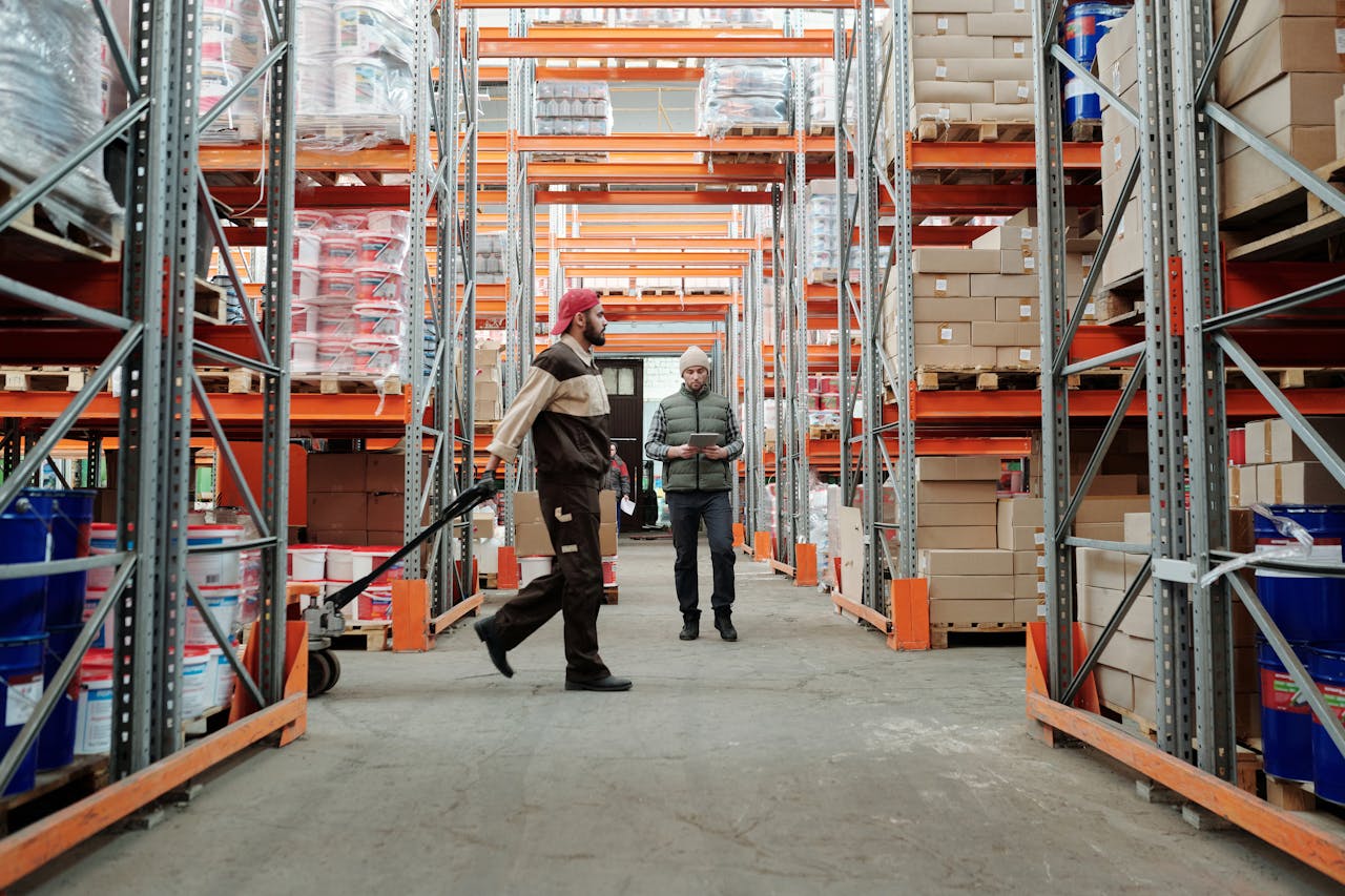 Two workers manage inventory in a spacious warehouse aisle.