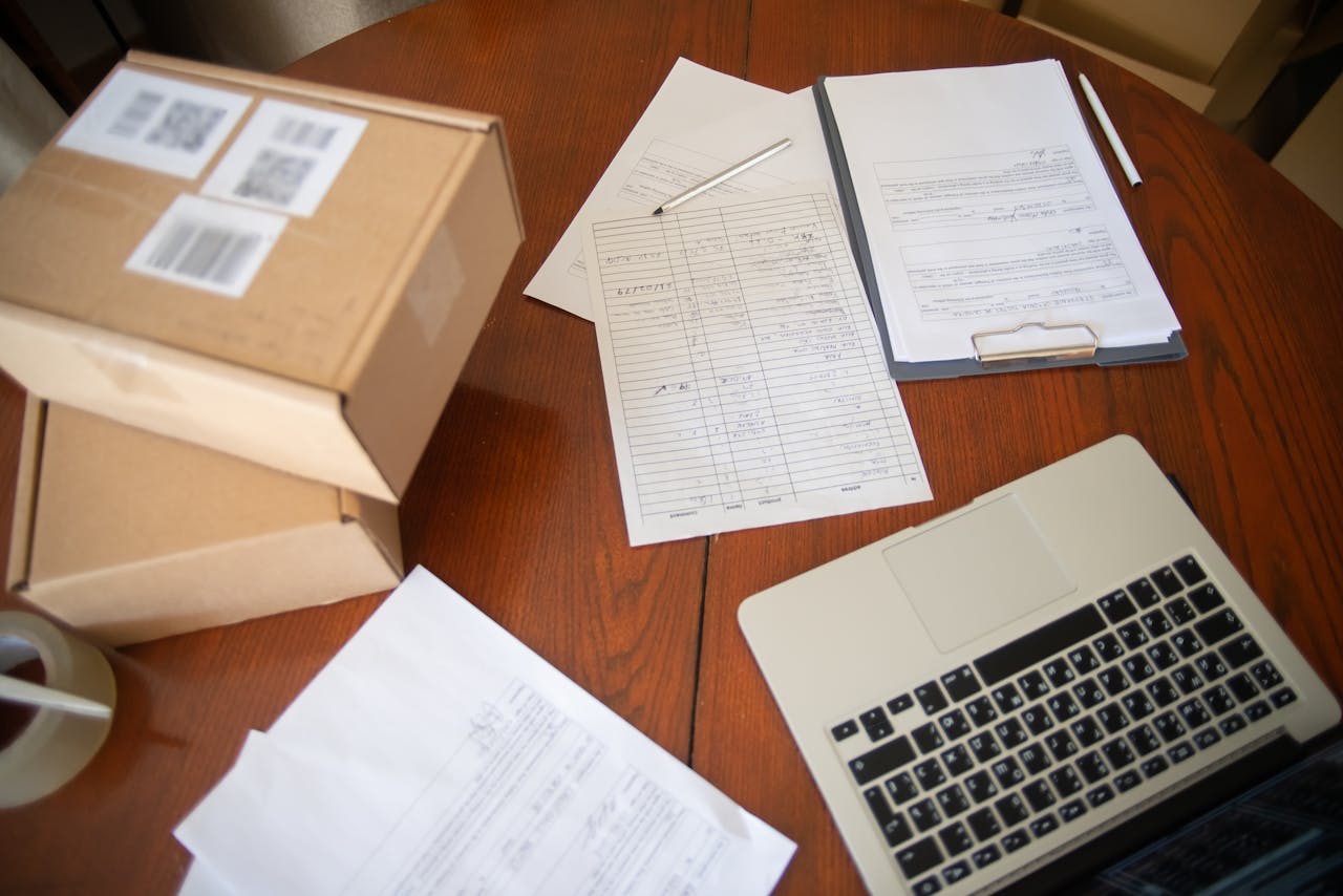 Flat lay of a workspace with laptop, documents, and cardboard boxes for e-commerce operations.